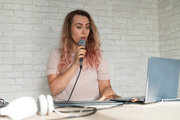 A woman records a vocal lesson using a laptop and accompanying on a keyboard while at home. The teacher sings a song into the microphone and plays the electronic piano. A blogger is recording a video. - Fotó, kép