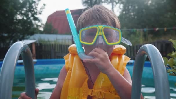 Sualtı maskeli küçük bir çocuk şişme havuzda yüzüyor ve ağzına bir tüp sokuyor. - Video, Çekim