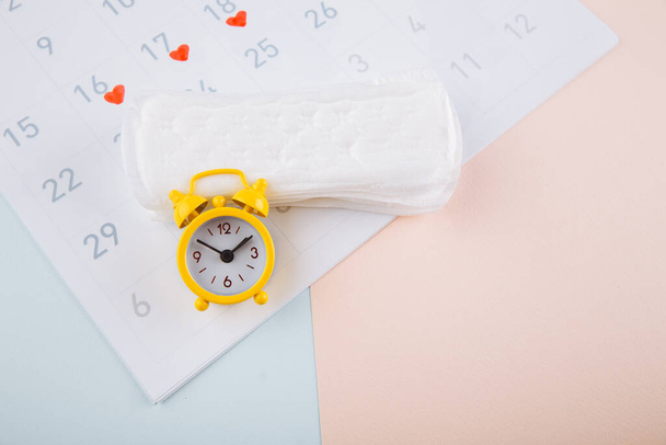 Calendário de menstruação com alarme amarelo e almofadas diárias no fundo rosa. Dias críticos da mulher, conceito de proteção de higiene da mulher
 - Foto, Imagem
