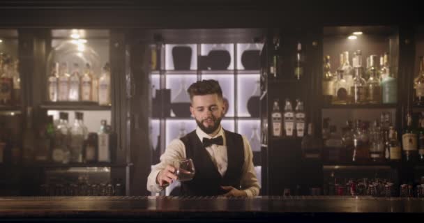 Il barista sta prendendo un bicchiere dallo scaffale e versando un drink nel bicchiere. 4K - Filmati, video