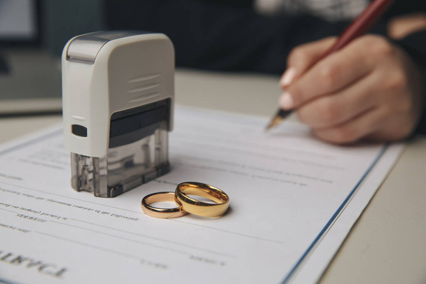 Χέρια συζύγου, συζύγου που υπογράφει διάταγμα διαζυγίου, διάλυσης, ακύρωσης γάμου, νομικών εγγράφων χωρισμού, κατάθεσης εγγράφων διαζυγίου ή προγαμιαίου συμβολαίου που εκπονείται από δικηγόρο. Βέρα γάμου - Φωτογραφία, εικόνα
