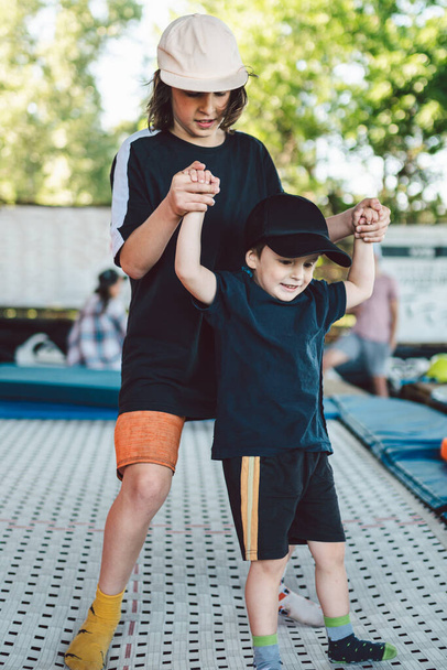 O irmão mais velho ensina o mais novo a saltar em um trampolim. Crianças de lazer ativo trampolining de mãos dadas. Fim de semana de esportes no centro esportivo de acrobacias e trampolim. Educação física
. - Foto, Imagem