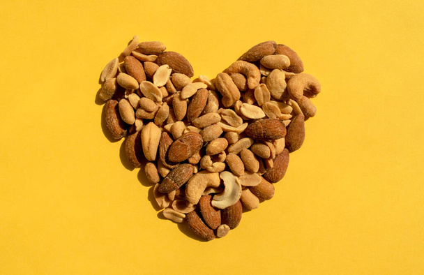 Různé ořechy ve tvaru srdce na žlutém pozadí. Horní pohled. Různé chutné a zdravé oříšky, svačinka. - Fotografie, Obrázek