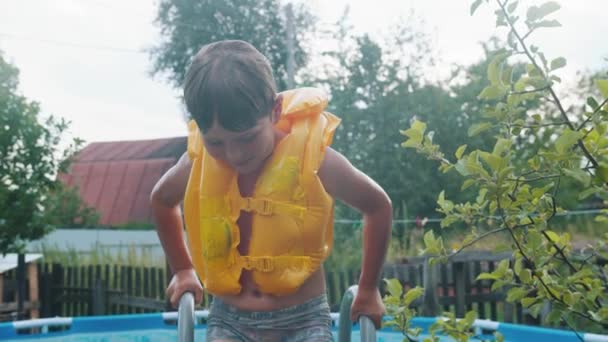 Un niño pequeño con chaleco salvavidas saliendo de una piscina inflable
 - Metraje, vídeo