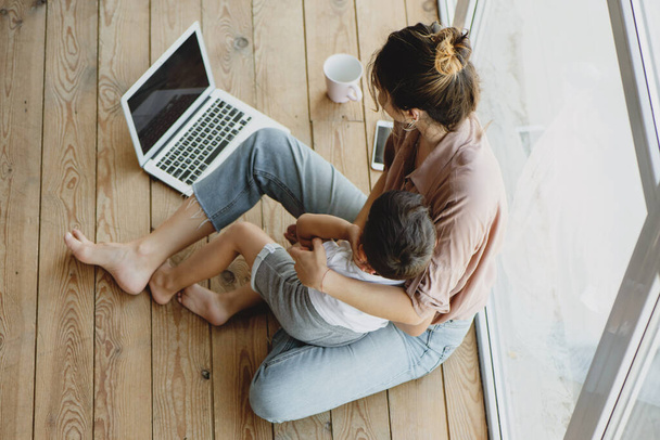 Young mom and her son sitting on floor and looking at laptop. - Foto, Imagem