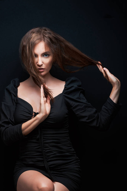 beautiful women in a dark dress posing on a dark background, beautiful brown hair holds hands - Foto, imagen