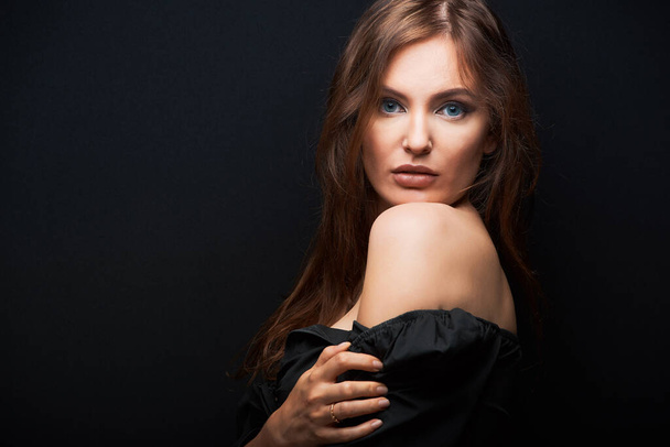 portrait of a beautiful woman in a dark dress posing on a dark background, beautiful brown hair looking from shoulder - Zdjęcie, obraz