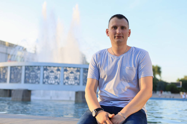 Un giovane caucasico in abbigliamento casual riposa seduto vicino alla fontana della città. - Foto, immagini