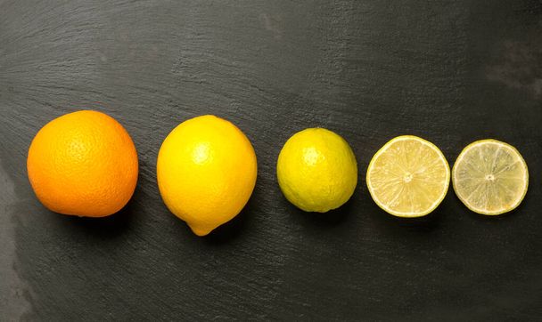 Close up of sliced citrus fruits orange, lemon and lime on dark black background. - Photo, Image