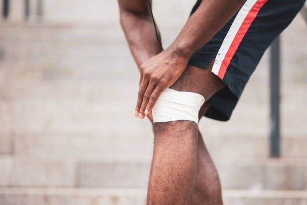 concept de blessure au genou, homme afro-américain bandant sa jambe avec un bandage, un homme blessé au genou à l'entraînement, gros plan - Photo, image