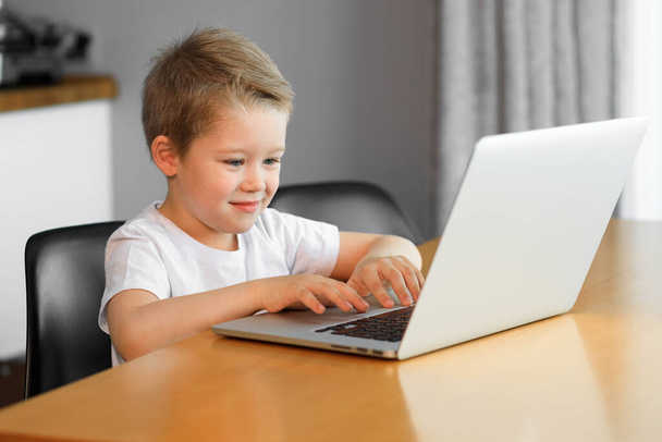 Funny young boy using a laptop computer sitting on top of a table at home - Photo, Image