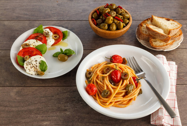 Full table of italian meals on plates. Spaghetti, caprese, olives and bread. - Photo, Image