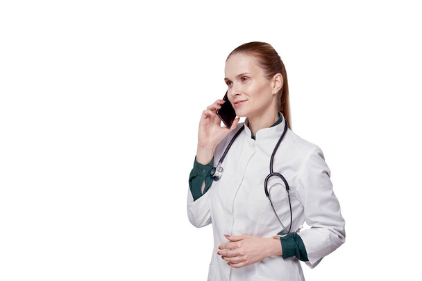 Female doctor talking on a cell phone in a white medical coat. - Фото, изображение