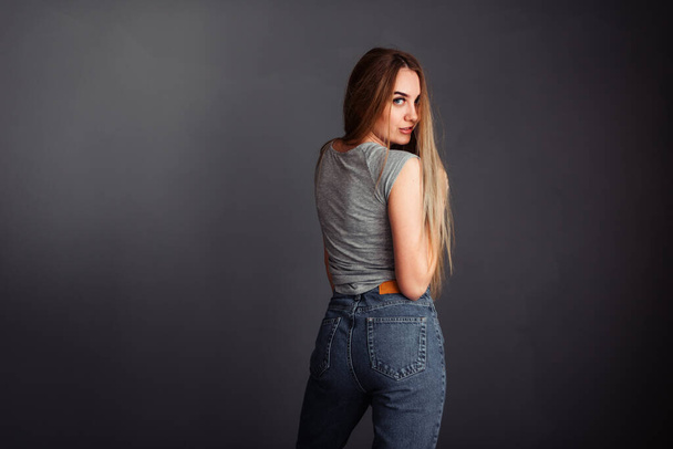 A girl with long hair looks from the back smiling at the camera, hands in front of him on a gray background without retouching. - Fotografie, Obrázek