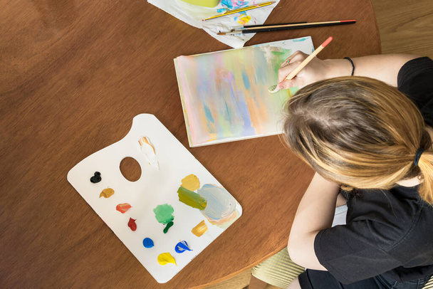 Teenager κορίτσι ζωγραφική με ακρυλικά χρώματα, κάθεται στο σπίτι, top view - Φωτογραφία, εικόνα