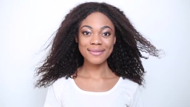 Egy fiatal, mosolygós afro-amerikai fiatal nő. A szél egy fekete lány haját fújja. Egy boldog, göndör hajú nő portréja. - Felvétel, videó