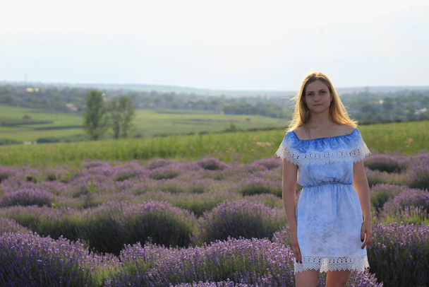 Lifestyle photo shoot in nature. A girl or young woman enjoys a walk through the fresh air and the scent of a lavender field in the sunset. Selective focus. - Фото, зображення