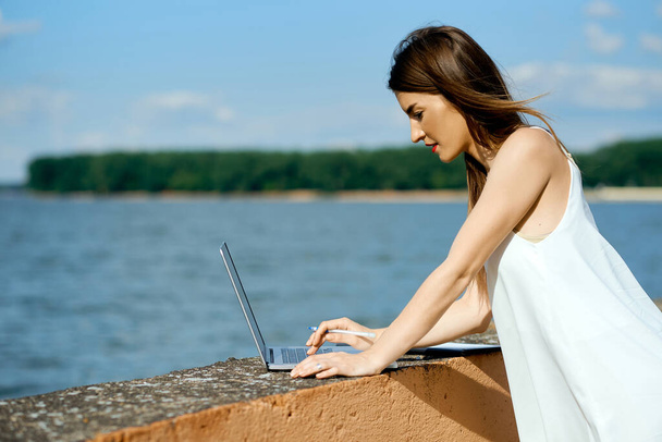красива, серйозна жінка в білій сукні з планшетом, ручкою, ноутбуком на причалі
 - Фото, зображення