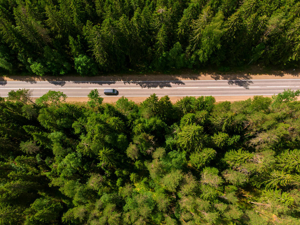 Samochód jedzie asfaltową drogą między zielonym lasem, widok z góry. - Zdjęcie, obraz