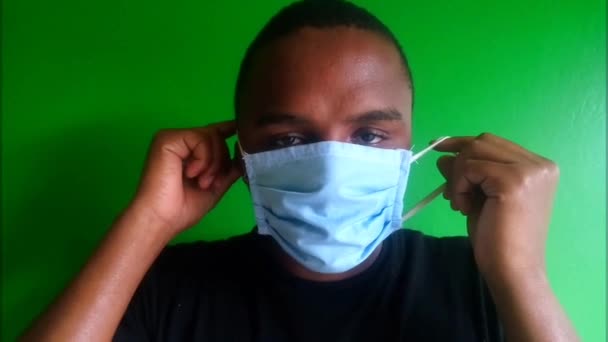 Man wearing a blue surgical mask footage. African. Black. Front view,close up. Straps over  ears. Adjusting face mask. Looking at camera. Protective gear for coronavirus,covid-19, 2019-ncov. Green background, green screen concept. Shadow. Chroma key. - Video