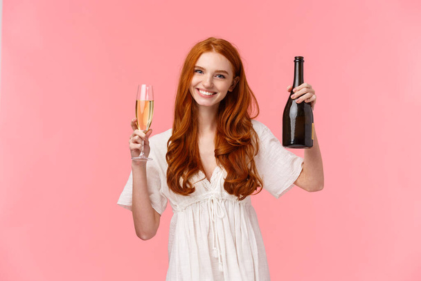 Вітаю, вітаю мого друга. Ніжна і щаслива, доброзичлива чарівна руда жінка в білій сукні, піднімає скло і тримає пляшку шампанського, відзначаючи успіх, рожевий фон
 - Фото, зображення