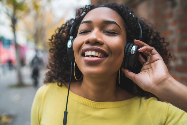 Portrait of Afro american woman smiling and listening to music with headphones in the street. Outdoors. - Φωτογραφία, εικόνα