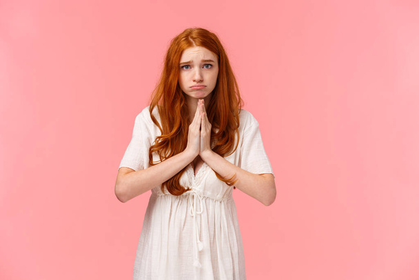 Gloomy and sad, cute pouting redhead girl asking for help, looking hopeful camera, make promise or appologizing, press hands together in pray, begging favour, pleading over pink background - Photo, Image