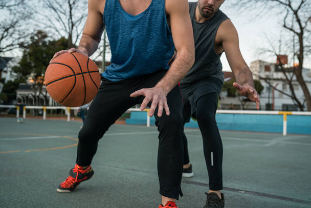 Young basketball players playing one-on-one on outdoor court. Sport and basketball concept. - 写真・画像