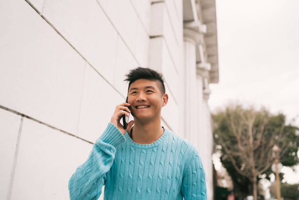 Portrait of young Asian man talking on the phone outdoors in the street. Communication concept. - Fotografie, Obrázek