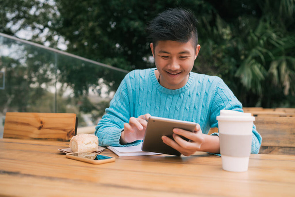 Portrait of young Asian man studying with his digital tablet while sitting in a coffee shop. Technology concept. - Foto, imagen