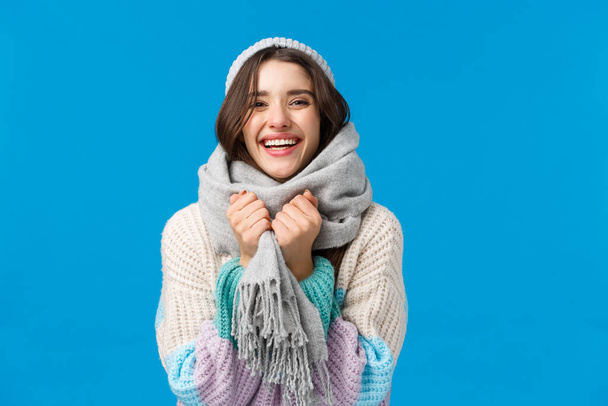 С праздником, наслаждаясь снежными днями. Счастливая и веселая харизматичная женщина в зимнем свитере, шляпе и шарфе, смеющаяся счастливо смотрящая в камеру, веселясь, стоя на синем фоне радостно
 - Фото, изображение