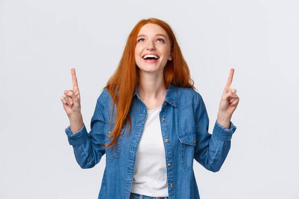 Cheerful charismatic redhead woman in denim shirt, looking and pointing up with happy smile, laughing, found exactly what need, dreaming, standing white background positive emotions - Φωτογραφία, εικόνα