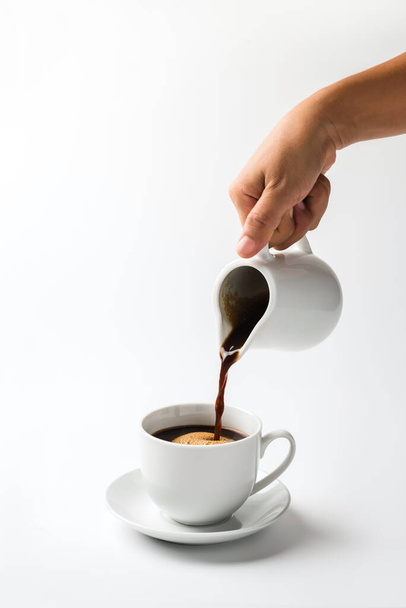 Ρίχνει καφέ σε ένα φλιτζάνι που απομονώνεται σε λευκό φόντο - Φωτογραφία, εικόνα