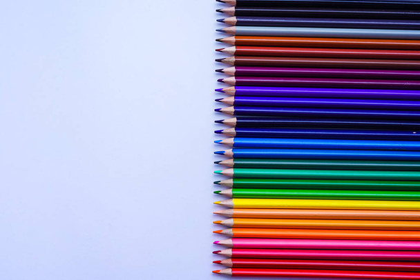 A set of their many colored pencils is laid out on a gray notebook in a row. Photo taken close-up on a white background in daylight. Left copy space - Foto, afbeelding
