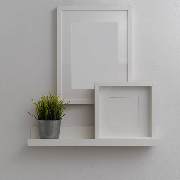Close up view of modern home interior design with mock-up frames and plant pot above white shelf on white wall  - Zdjęcie, obraz