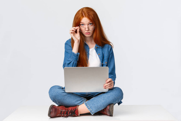 Excuse me what, I am busy. Questioned redhead female student interrupted during preparing project, searching material for class in internet, look curious camera, sitting on floor with laptop - Photo, Image