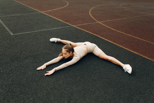 A sporty woman trains and exercises at a fitness stadium. Warm-up in the open air, stretching. - Photo, Image