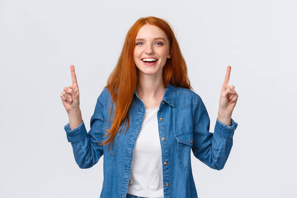 Cheerful outgoing alluring redhead woman, long red hairstyle, showing top promo, pointing fingers up and laughing, smiling amused, leave positive review, blogger visit awesome place, white background - Fotografie, Obrázek