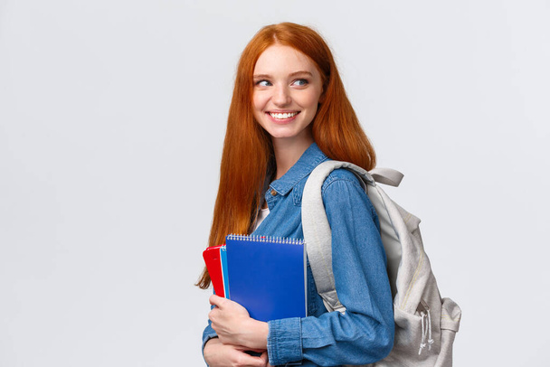 Girl seeing classmate in hall saying hi, turning back to greet someone, smiling joyfully, holding backpack and notebooks, heading back to class, studying in college, standing white background - Foto, imagen