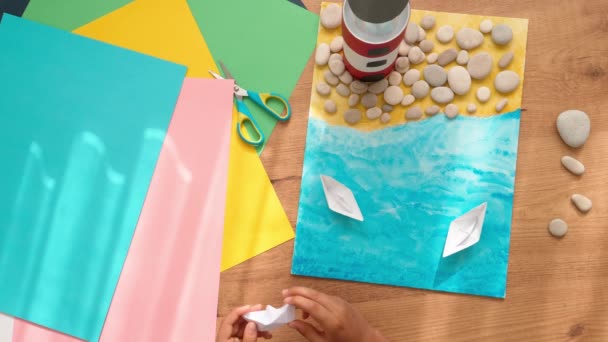 Kid hands make a lighthouse for school project at home. Top down view to the table with colored paper and other supplies - Footage, Video