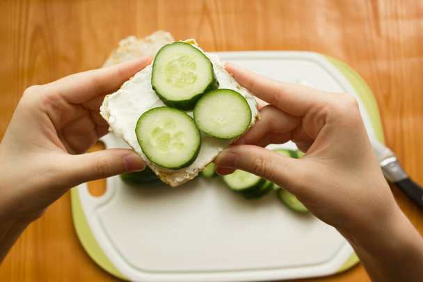 Sağlıklı bir kahvaltı sandviçi hazırlamak için talimatlar. İkinci adım salatalıkları krem peynirin üzerine koy. Sağlıklı kahvaltı, organik krem peynirli ve salatalıklı çıtır ekmek.. - Fotoğraf, Görsel