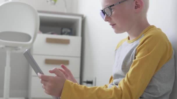 Un garçon avec des lunettes avec un occluder joue dans une tablette à la maison - Séquence, vidéo