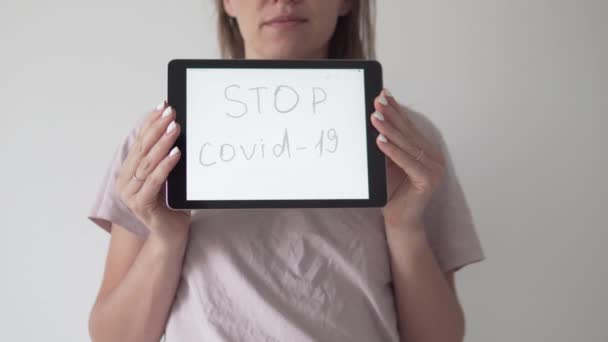 Een vrouw houdt een tablet op het scherm in grote letters opschrift STOP Covid-19 - Video