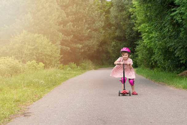 Portrait of active little toddler girl riding scooter on a village road outdoors - Zdjęcie, obraz