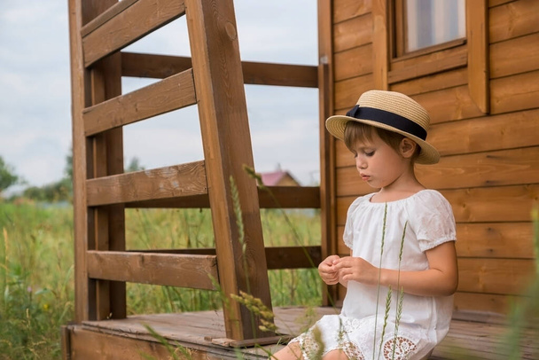 Little girl in a white boho dress and a hat against the background of a house. - Photo, Image