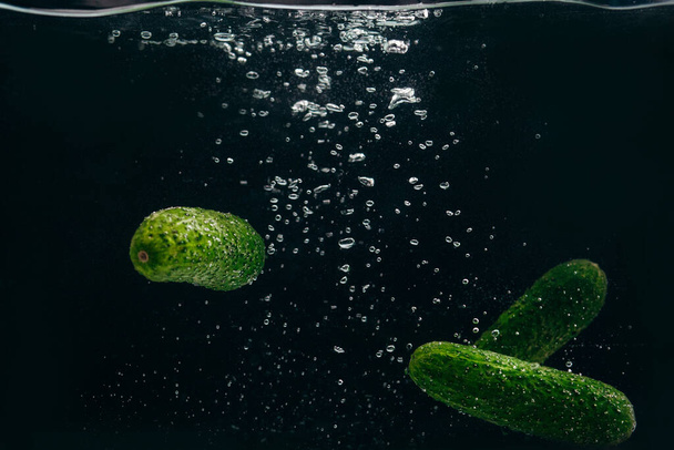 Concombres verts dans l'eau sur fond noir. - Photo, image