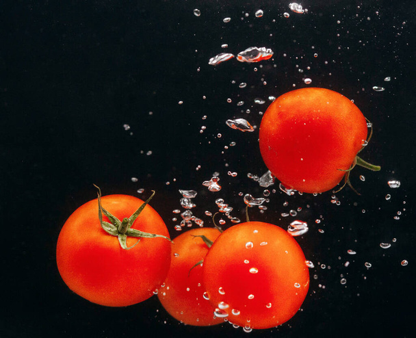 Червоні помідори у воді на чорному тлі
. - Фото, зображення