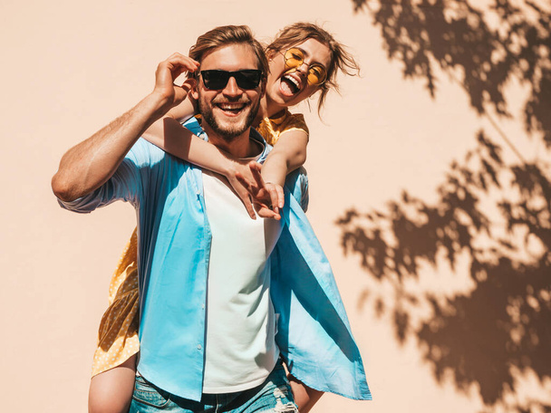 Portrait of smiling beautiful girl and her handsome boyfriend. Woman in casual summer dress and man in jeans. Happy cheerful family. Female having fun in the street near wall - Photo, Image