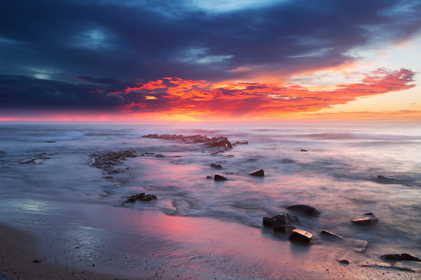 Sonnenaufgang über dem Ozean mit Felsen und Wasser im Vordergrund - Foto, Bild