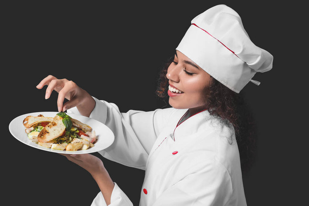 Female African-American chef with tasty dish on dark background - Photo, Image